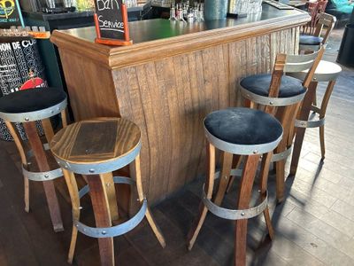 trois tabourets en bois disposés devant un bar, avec un tableau noir accroché au mur