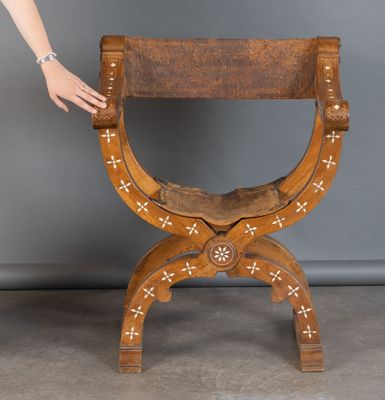 une personne tendant la main vers une chaise en bois ornée de croix