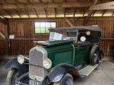 une vieille voiture verte dans un garage au toit en bois