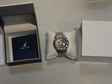 une montre dans une boîte posée sur une table, à côté d'un coffret à montres