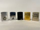quatre briquets Zippo différents posés côte à côte sur une surface blanche