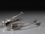 deux cuillères en argent et une pince posées sur une surface blanche