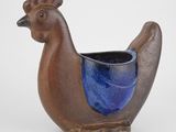 un vase en forme d'oiseau, de couleur marron et bleue, posé sur un fond blanc