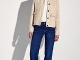 the woman is wearing a jacket and jeans standing in front of a white wall