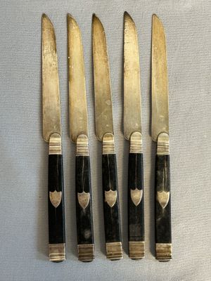 four knives with black handles and gold accents on a white surface