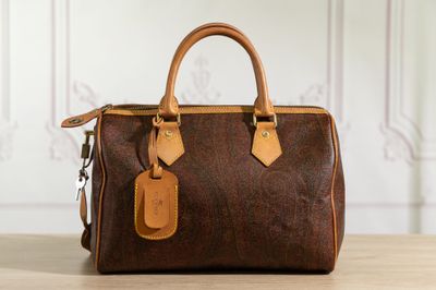 the brown and tan handbag is sitting on a wooden table