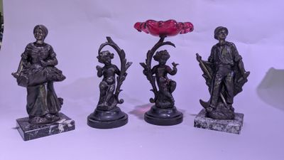 quatre statues en bronze représentant des personnages et une fleur sur fond blanc