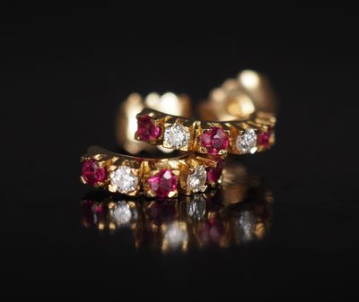 une paire de boucles d'oreilles créoles en rubis et diamants posées sur un fond noir