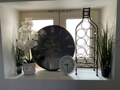 une horloge posée sur le rebord d'une fenêtre, à côté d'une plante en pot