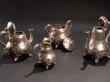 three silver teapots and a sugar bowl on a black surface