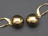 une paire de boucles d'oreilles en forme de boules dorées posées sur une surface noire