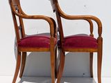 two wooden chairs with red upholstered cushions against a white wall