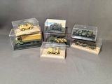 Plusieurs véhicules militaires miniatures sont exposés dans des boîtes transparentes posées sur une surface grise.