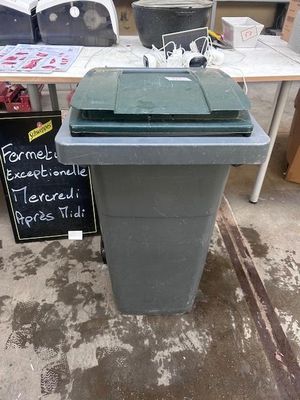 a green trash can sitting on the floor in front of a table