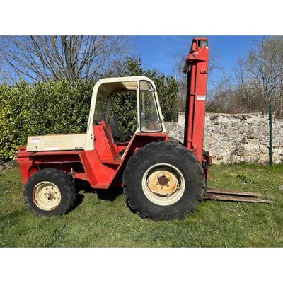 a red tractor parked in the grass near a stone wall