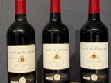 three bottles of wine sit on a wooden table in front of a gray wall