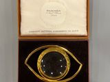 an image of a gold and black eye shaped broochle in a box