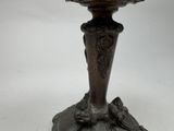 a silver vase with a bird on it on a table