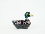un petit canard noir et doré posé sur une surface blanche