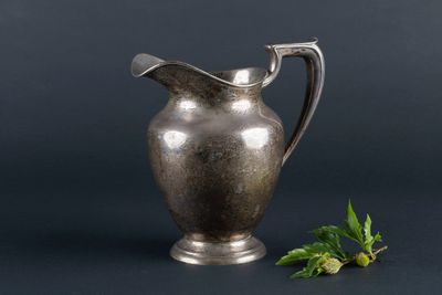 an antique silver pitcher with a sprig of mint on a black background