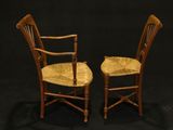 pair of wooden chairs with wicker seats against a black background