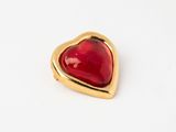 a close up of a red heart shaped broochle on a white surface