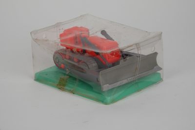 un tracteur miniature dans une boîte transparente posée sur un socle vert