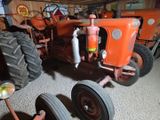 an orange tractor sitting in a garage next to a red tractor