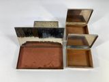 three small silver boxes with mirrors on top of them on a white surface