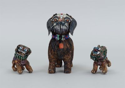 trois figurines miniatures représentant des chiens portant des colliers colorés, posées sur une surface blanche