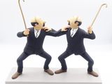 two figurines of two men in suits with canes on a white surface