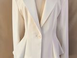 un blazer blanc posé sur un mannequin, devant un fond beige