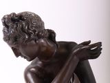 bronze statue of a boy sitting on a rock with his hands on his knees