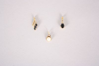 three pairs of gold earrings with black stones on a white surface