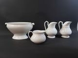 three white pitchers and a bowl on a black table