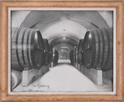 photographie en noir et blanc de tonneaux de vin alignés dans une cave