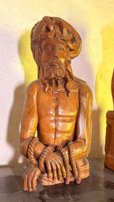une statue en bois représentant un homme assis sur une table, à côté d'un vase