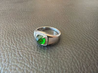 silver ring with a green stone and diamonds on a leather surface