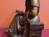 une statue représentant une femme assise sur un banc en train de lire un livre