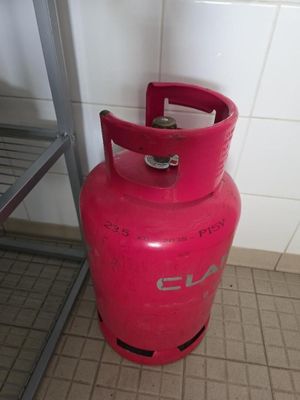 une bouteille de gaz rouge posée par terre à côté d'une étagère