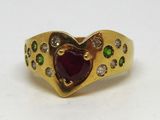 une image représentant une bague en or sertie d'une grenat en forme de cœur, entourée de pierres vertes et blanches
