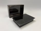 une boîte noire surmontée d'un miroir, posée sur une surface blanche