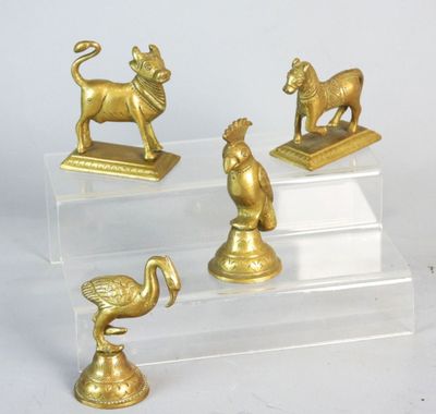 three gold figurines of animals and a bird on a clear base