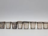 six verres à shot en argent alignés en rangée sur une surface blanche