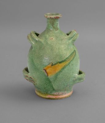 a green vase with a yellow handle sitting on a gray surface