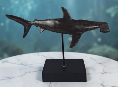 une photo d'une sculpture en bronze représentant un requin, posée sur une table en marbre
