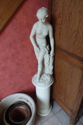 une statue représentant une femme debout sur un socle, à côté de toilettes