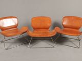 trois fauteuils en cuir orange et une table basse sur fond gris