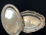 two silver plated dishes sitting on a stand on a black surface