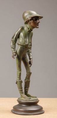 statue en bronze représentant un garçon portant un chapeau et une veste, posée sur une table en bois